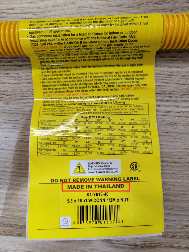 Close-up view of the yellow label on the recalled gas connector with "Made in Thailand" listed on label